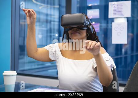 At modern office for business, young biracial woman is wearing virtual reality headset Stock Photo