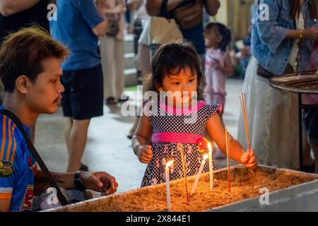 Bangkok, Thailand. 22nd May, 2024. A kid holds incense sticks during the candlelight procession, on Visakha Bucha day, at Lat Phrao Temple, situated in a low-income community, in Bangkok, Thailand. Visakha Bucha, one of Thailand's most important Buddhist holidays, commemorates the birth, enlightenment, and passing of Gautama Buddha, all on the same date. Thai Buddhists typically visit temples to make merit, which involves activities such as giving alms to monks, listening to sermons, and participating in various religious rituals. Credit: SOPA Images Limited/Alamy Live News Stock Photo