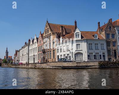 Row of adjacent historic buildings with tiled roofs by the river under clear sunshine and blue sky, old historic houses with church towers and Stock Photo