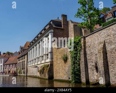 Historic riverside buildings with brick walls and windows under a sunny blue sky, old historic house facades with towers and bridges by a river Stock Photo