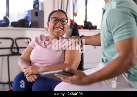 A biracial female paraplegic patient smiling at gym rehab center with therapist Stock Photo