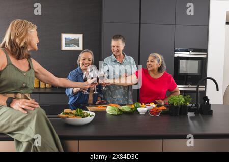 Diverse senior female friends enjoying drinks at home in kitchen Stock Photo