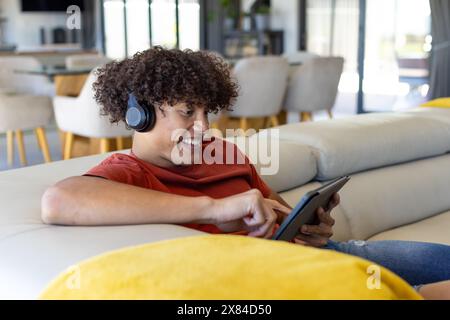 A biracial young male wearing headphones, holding tablet at home Stock Photo