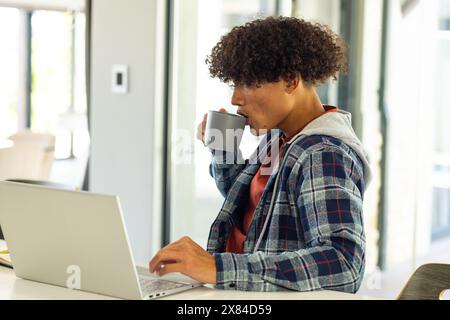A biracial young male drinking coffee, using laptop at home Stock Photo