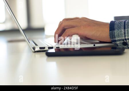 A biracial young male at home, wearing plaid shirt, typing on a laptop Stock Photo