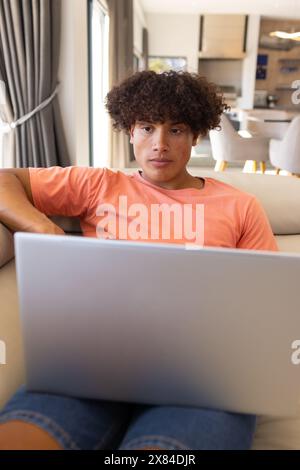 A biracial young male using laptop at home, sitting on a sofa Stock Photo