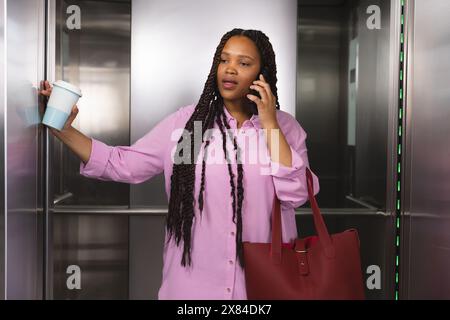 At modern office for business, young biracial woman stands in elevator on her phone Stock Photo