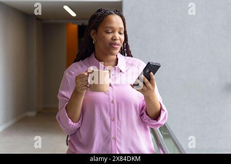 At modern office for business, young biracial woman in hallway holding mug Stock Photo