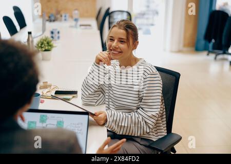 Two smiling female freelancers talking during work on laptop while sitting in cozy coworking Stock Photo