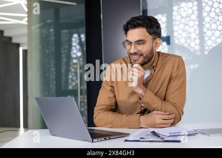 Young professional focused on his laptop while working in a contemporary office space. Business concepts and productivity captured. Stock Photo