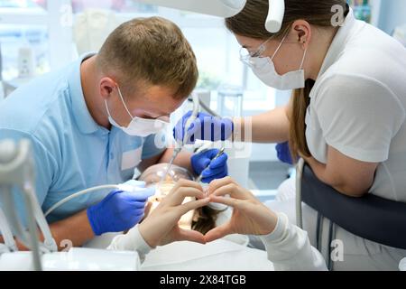 Dentist with assistant under microscope treats the patient's teeth. Modern progressive dentistry. Professional tooth cleaning Stock Photo