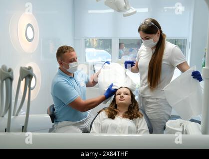 Dentist with assistant under microscope treats the patient's teeth. Modern progressive dentistry. Professional tooth cleaning Stock Photo