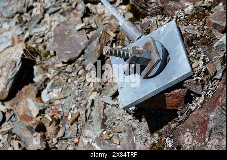 A large bolt and square plate has been driven into the ground to hold a cable. Stock Photo