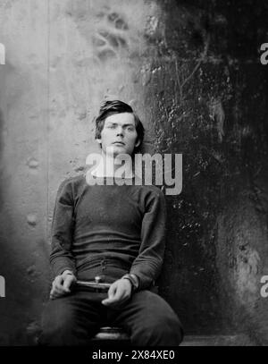 Lewis Powell (aka Lewis Payne), in sweater, seated and manacled, one of the conspirators in the Abraham Lincoln assassination. This photograph has background of dark metal, and was presumably taken on U.S.S. Saugus, where he was for a time confined. Washington Navy Yard, District of Columbia. 27 April 1865. By Alexander Gardner. Stock Photo