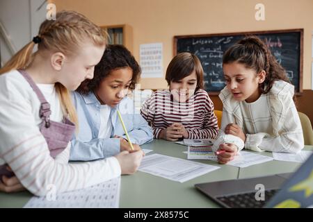 Group of ethnically diverse boys and girls sitting at table in classroom doing exercise during lesson at school Stock Photo
