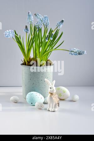 Easter composition with white rabbit, eggs and light blue muscari flowers in cup. Easter still life Stock Photo