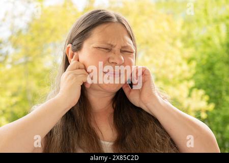 caucasian mature woman holds painful ear, hearing loss, face close-up, medical concept, hearing control, middle ear inflammation, otitis media Stock Photo