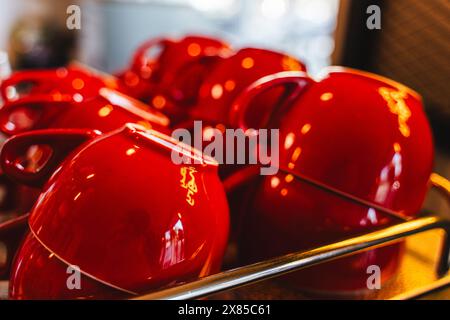 Many ceramic red coffee cups on a coffee machine shelf in a cafe. Selective focus. Red coffee cups on a shelf in a cafe, second row of selective red c Stock Photo