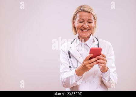 Portrait of mature female doctor using mobile phone  on gray background. Stock Photo