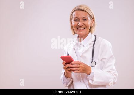 Portrait of mature female doctor using mobile phone  on gray background. Stock Photo