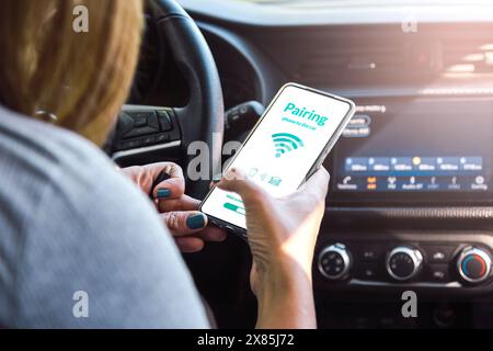 Pairing car with phone.Woman using mobile device while driving. Connecting car computer to her smartphone and app using wireless technology. Stock Photo