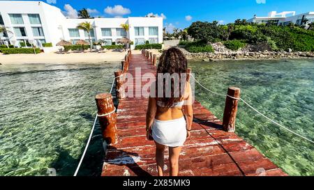Woman walking along the pier of a paradisiacal beach in the Riviera Maya (Mexico), this dock is on a crystal clear turquoise water that leads to the w Stock Photo