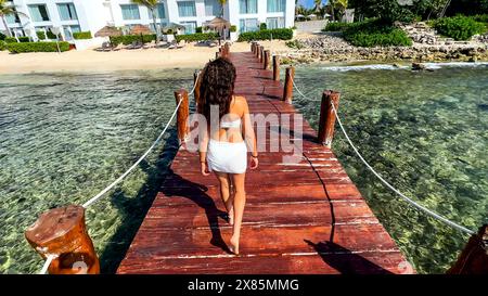 Woman walking along the pier of a paradisiacal beach in the Riviera Maya (Mexico), this dock is on a crystal clear turquoise water that leads to the w Stock Photo
