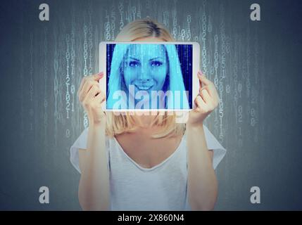 Happy woman holding tablet with her face displayed on a screen with binary code Stock Photo