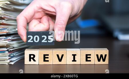 Wooden cubes form the expression '2025 review' next to a pile of paper. Stock Photo