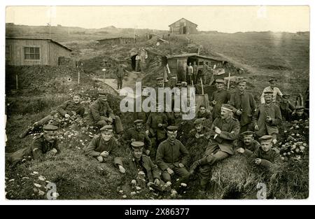 Original and very clear WW1 era postcard of German soldiers relaxing in a trench near buildings, fortified dugout, behind the lines, unknown date or location. Full of characters, wearing infantry soldier uniform, boots, field cap (kratzchen), some smoking a pipe.  Europe, possibly France. 1914-1918 Stock Photo