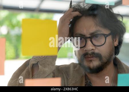 A man thinking and writing on sticky note on the wall. Stock Photo