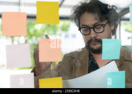 A man thinking and writing on sticky note on the wall. Stock Photo