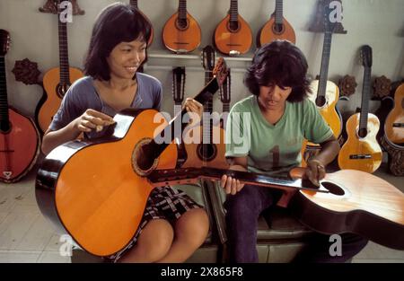 Philippines, Cebu; Mother and son polish newly made guitars in a factory where guitars are made. Stock Photo