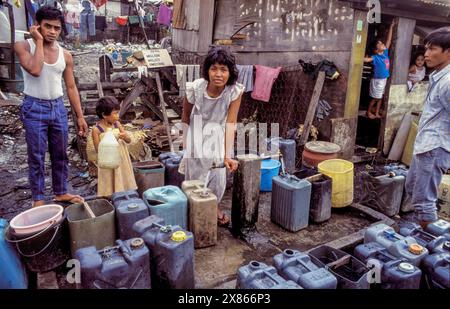 Philippines, Manila; A mother fills jerrycans with drinking water in a slum. Stock Photo