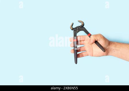 Man hand holding pincers on a light blue background with copy space Stock Photo