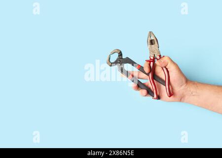 Man hand holding pliers and pincers on a light blue background with copy space Stock Photo