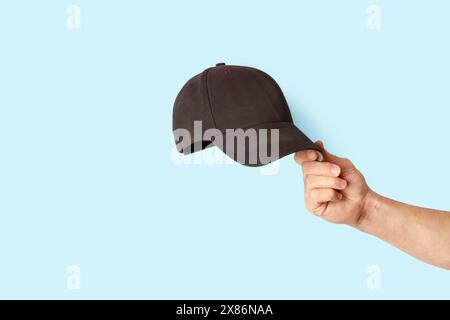 Man hand holding a black sports cap isolated on a blue background Stock Photo