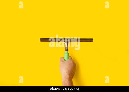 Man's hand holding a glass cleaner on a yellow background with copy space Stock Photo
