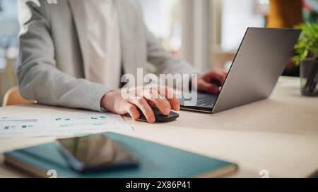 Manager Sitting at a Desk in Creative Office. Focus On Hands of a Young Stylish Man in a Jacket Using Laptop Computer in Marketing Agency. Employee Typing and Using Mouse Stock Photo