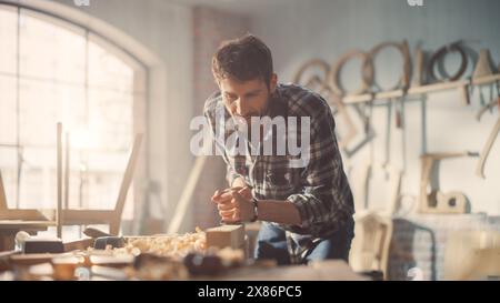 Close Up Portrait of a Handsome Young Artisan Craftsman in Checkered Shirt Using Hand Plane to Shape a Wood Bar. Carpenter Working on a Project in a Loft Studio with Tools on Walls. Stock Photo