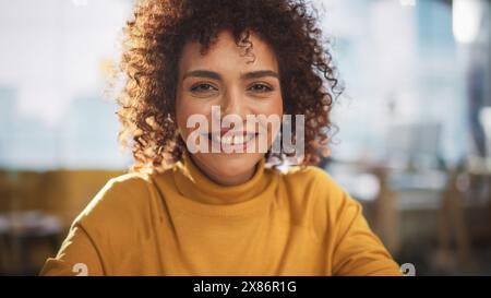 Portrait of an Attractive Arab Female in Creative Agency. Young Stylish Manager with Curly Hair Smiling, Looking at Camera. Manager Working in Modern Company. Stock Photo