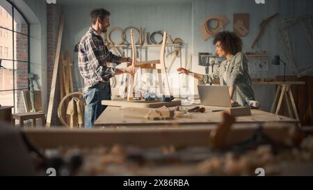 Small Business Owners of a Furniture Store Working on a New Wooden Dining Table Chair. Carpenter Building the Chair, While Young Female Manager Using Laptop Computer. Stock Photo