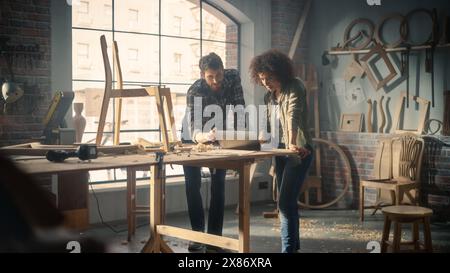 Portrait of Happy Young Business Couple Using Laptop Computer in Designer Furniture Studio. Carpenter and Designer Have Fun, DIscussing and Talking About Upcoming Orders of Wooden Furniture. Stock Photo
