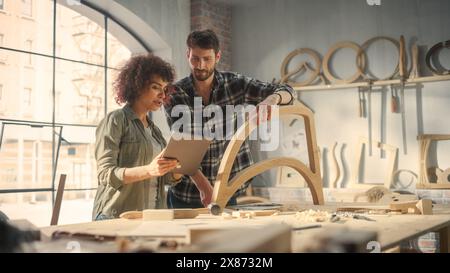 Small Business Owners of a Furniture Workshop Using Tablet Computer and Discussing the Design of a New Wooden Chair. Handsome Carpenter and Young Female Apprentice Working in Loft Studio. Stock Photo