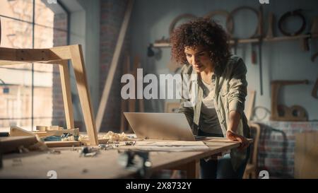 Multiethnic Artisan Arab Woodworker Using Laptop Computer and Building a Wooden Chair. Black Multiethnic Female Carpenter Working in a Studio in Loft Space with Tools on the Walls. Stock Photo