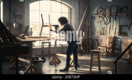 Multiethnic Artisan Woodworker Entering Loft Studio, Starting to Work on a Wooden Chair with an Electric Drill. Black Female Carpenter Working in Workshop with Tools on the Walls. Stock Photo