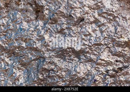 The rough and wrinkled concrete wall is painted with rose silver shining paint. Horizontal photo. Stock Photo