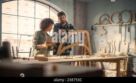 Excited Young Man and Woman Using Tablet Computer, Discussing a Successful Project in a Carpentry Studio. Furniture Designers Working in Loft Studio. Stock Photo