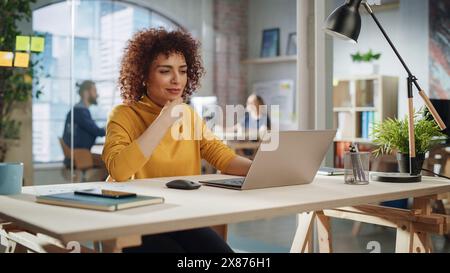 Confident Arab Female Sitting in Creative Agency, Manager Working on Implementing Modern Business Strategy for Client. Excited Specialist Writing Corporate Project Plans on Laptop Computer. Stock Photo