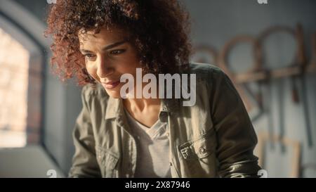 Close Up Portrait of a Multiethnic Artist Using Laptop Computer. Black Creative Female Typing Emails, Browsing Internet, Making an Online Project in a Loft Studio with Tools on the Walls. Stock Photo